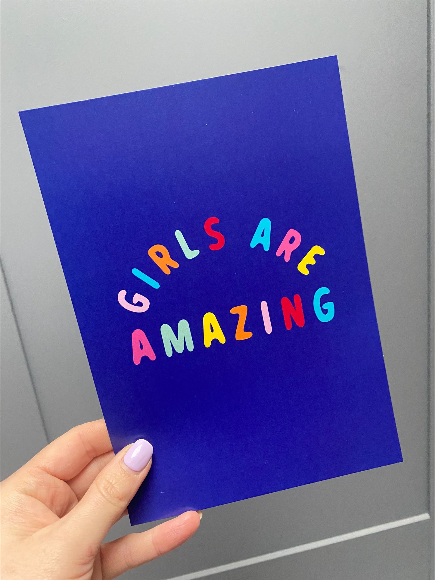 girls are amazing blue poster, a navy blue with coloured text poster being held in a hand