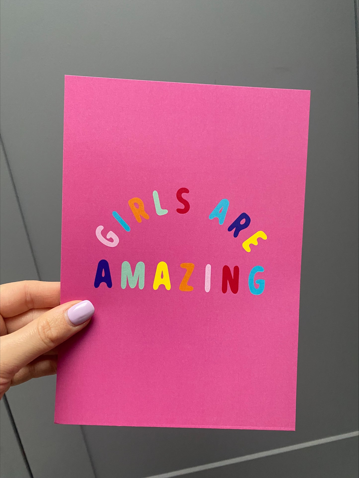 girls are amazing pink poster, a pink ground colour with multi-coloured text poster being held by a hand