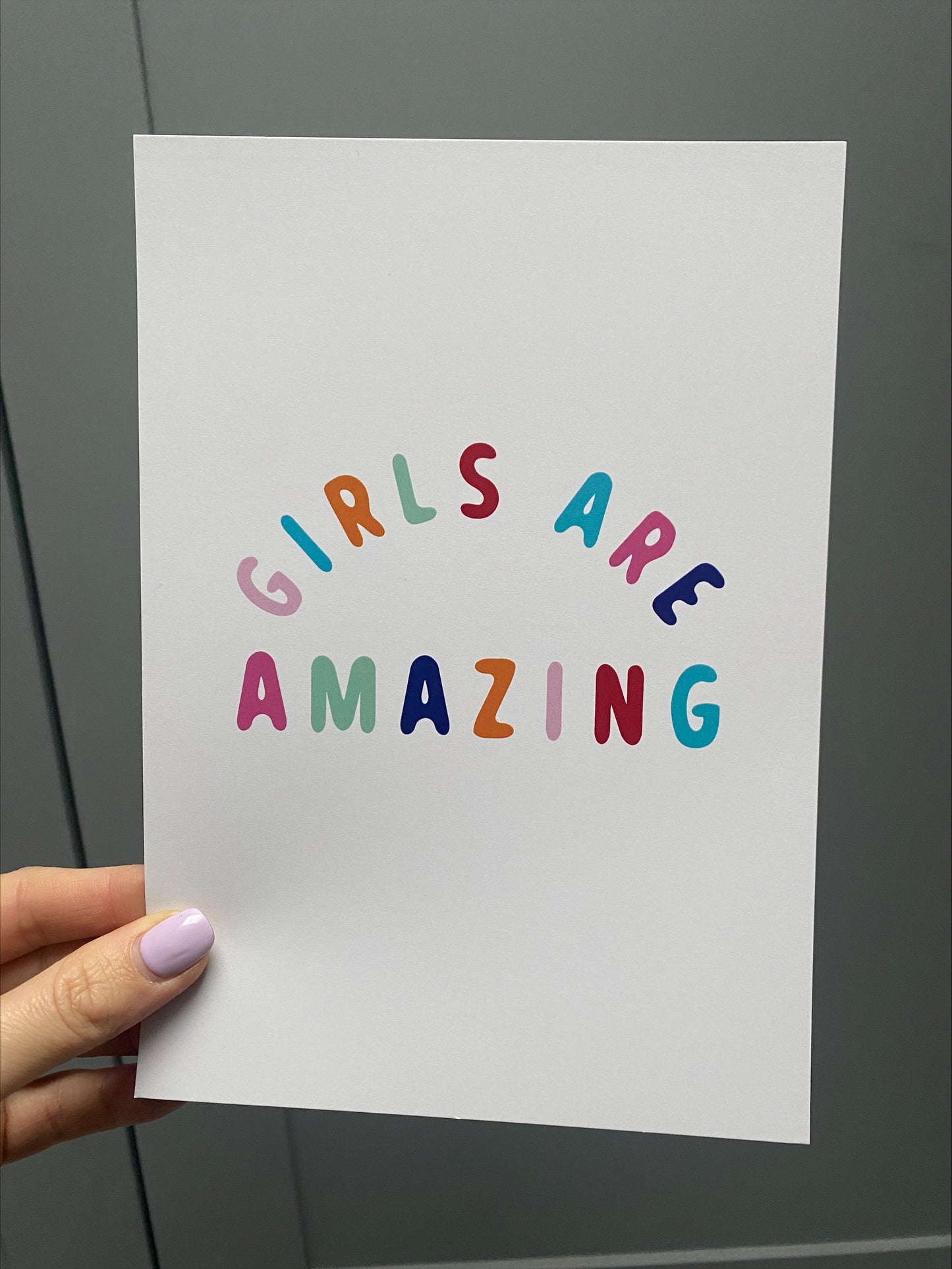 girls are amazing white poster, a white ground colour with multi-coloured text poster being held by a hand