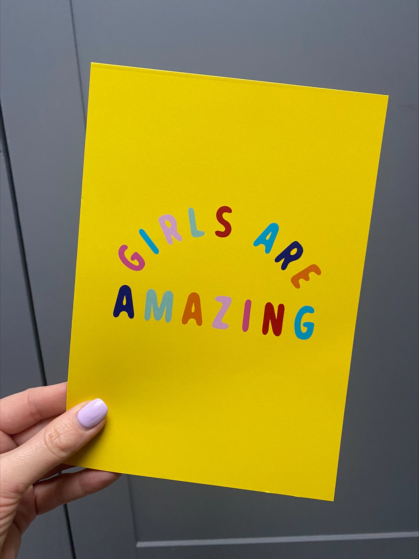 girls are amazing yellow poster, a yellow ground colour with multi-coloured text poster being held by a hand