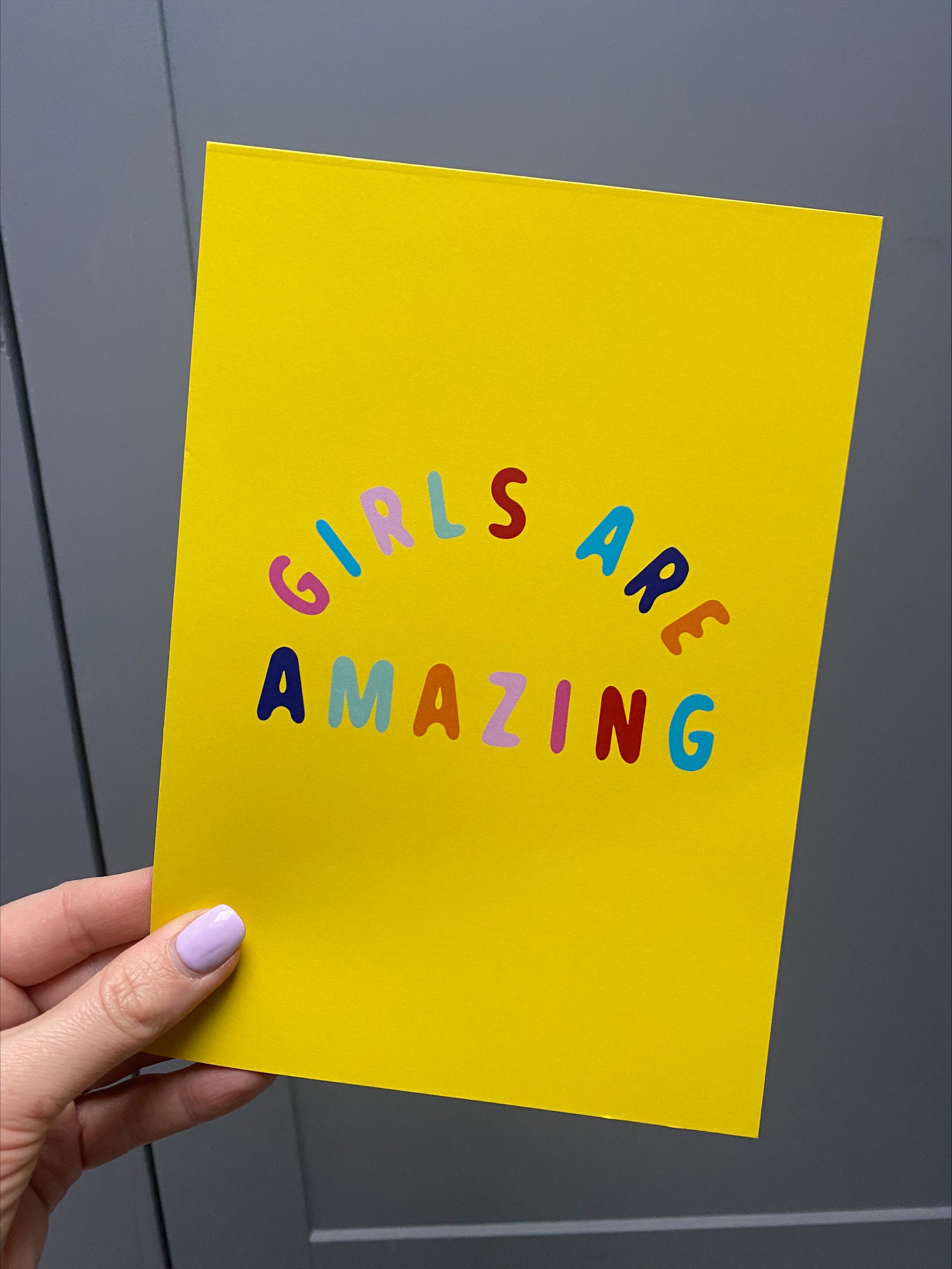 girls are amazing yellow poster, a yellow ground colour with multi-coloured text poster being held by a hand